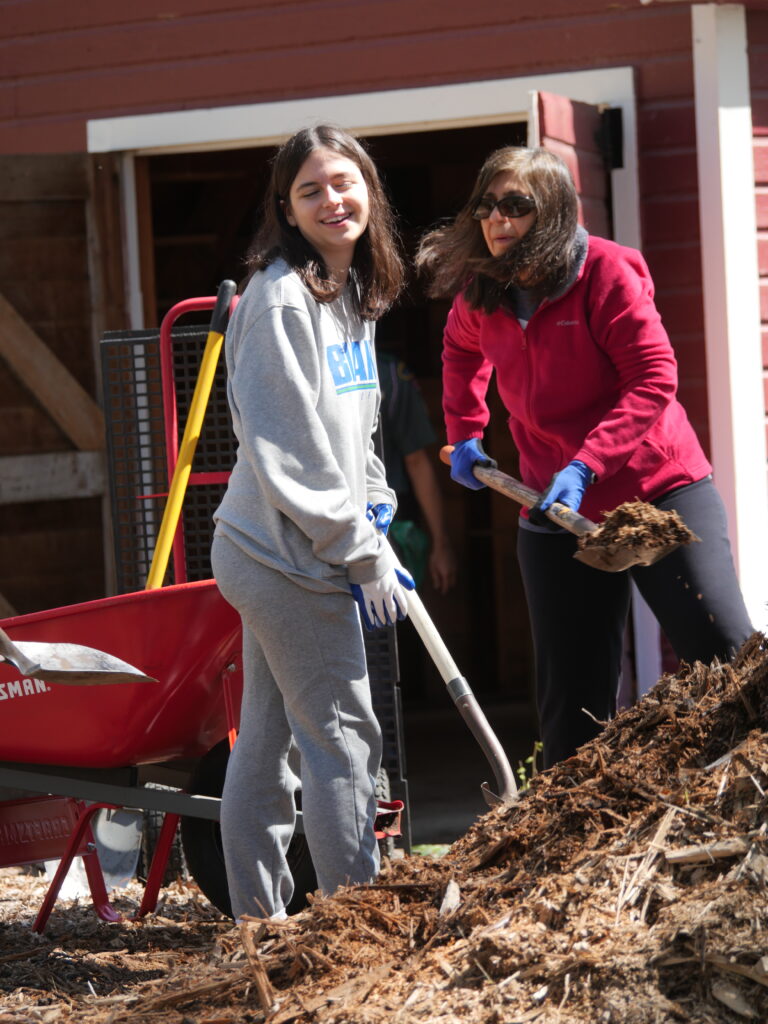 Mother and daughter working together to fill a wheelbarrow with woodchips during Green Crew’s trail maintenance on the Nicollet Trail, promoting Leave No Trace access for science-based conservation projects.